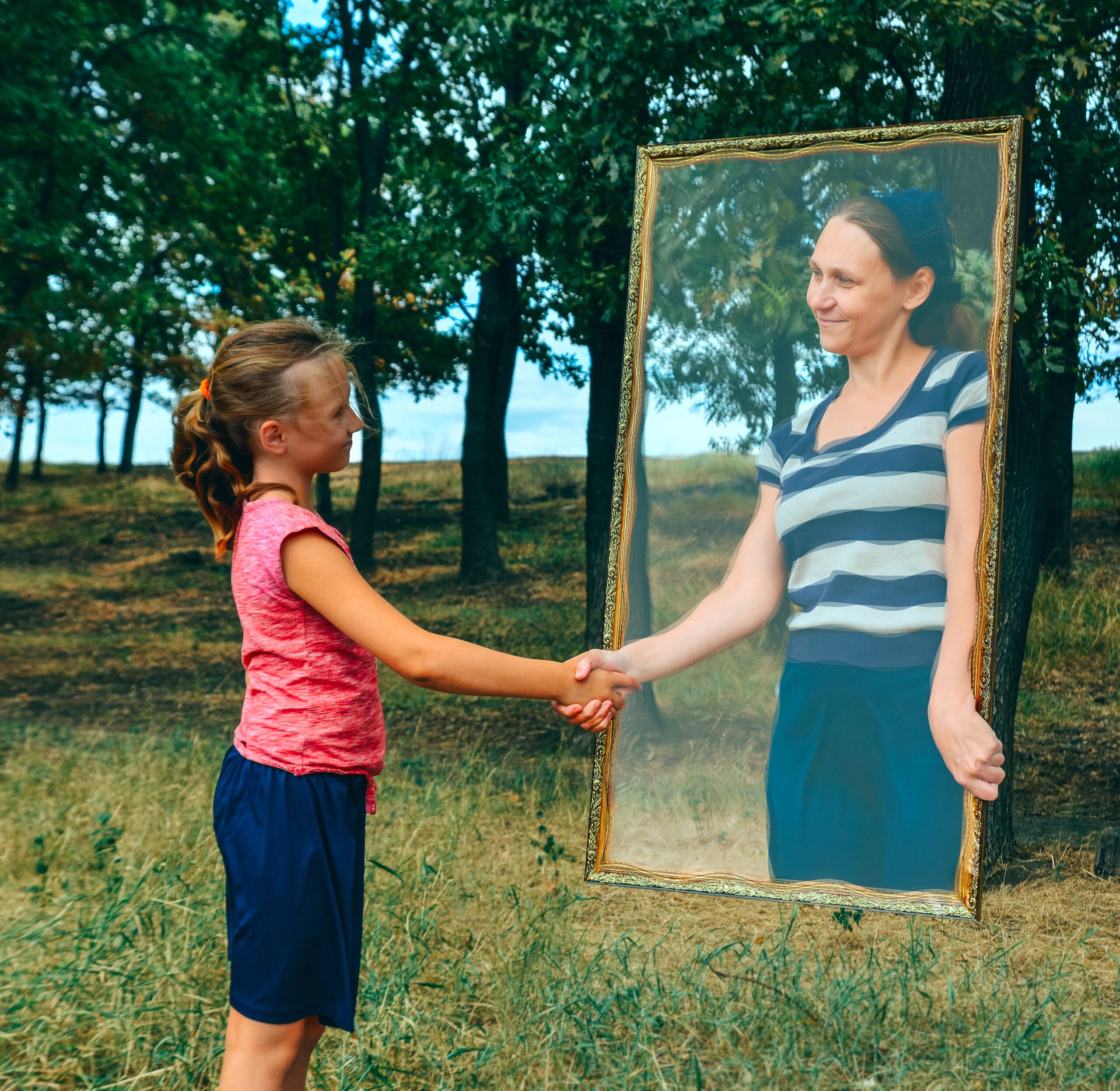 An image of a person inside a mirror, reaching out to shake hands with a person standing in a field with trees. They are clearly different people but both share a similar gender presentation.